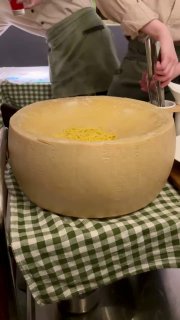 Головка пармезана на столе ресторана с натёртым сыром внутри, на клетчатой скатерти, видны руки официанта, подача блюда