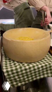 Большая круглая головка пармезана на столе в ресторане, из которой готовят и подают пасту прямо в сырной чаше, процесс сервировки