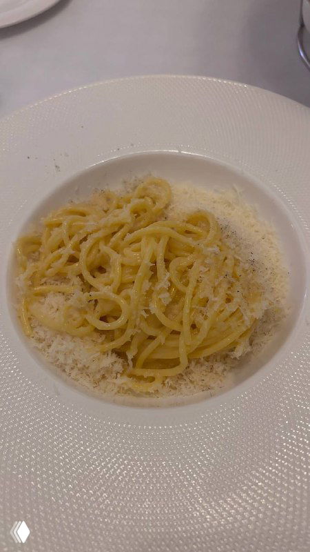 Тарелка пасты, аккуратно уложенные спагетти с тёртым сыром, снятые крупным планом на фоне столовой посуды ресторана