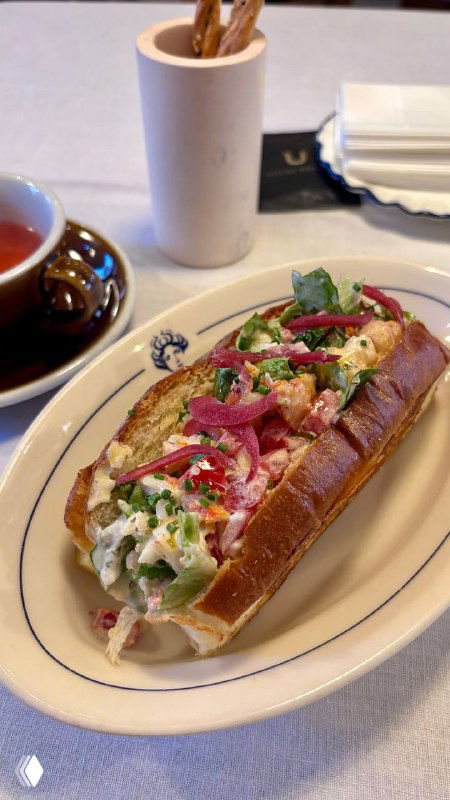 Крупный план краб‑бриоши: мягкая бриошь с начинкой из краба, листья романо, ломтики томата и кремовая заправка, сервировка на белой тарелке в кафе.