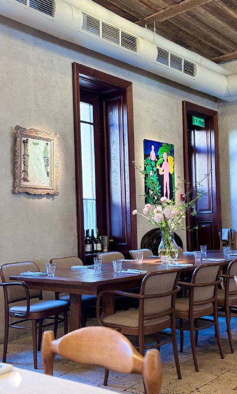 Другая панорамная зона зала Mamie: длинный стол, современная художественная картина на стене и букет цветов на столе, вид крупным планом.