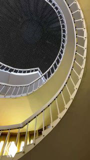 Фрагмент спиральной лестницы с изгибом ступеней и перил, акцент на переходах света и тени по кривой поверхности внутри библиотечного интерьера.