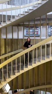 Женщина поднимается по одной из лестниц библиотеки, видно перекрытие балюстрад и информационные таблички на стенах в глубине кадра.