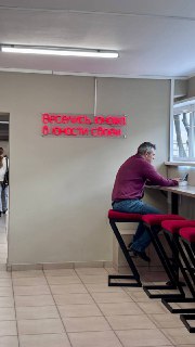 Неоновая надпись на стене столовой и посетитель у стойки, интерьер столовой и минималистичная обстановка с девизом юности.
