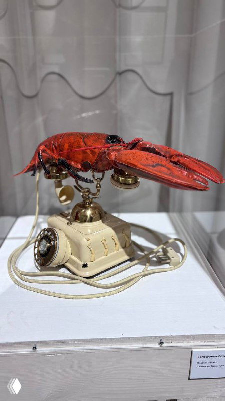 Фото экспоната: телефон-лобстер Сальвадора Дали в витрине выставки, ярко-красный корпус, виден дисковый телефон и детали механизма