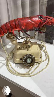 Крупный план телефон-лобстера — арт-объект Дали с красной панцирной формой и винтажным телефоном, экспонат на белой подставке в музее