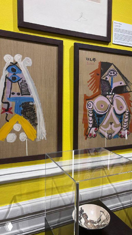 Стена с маленькими портретами в рамках, работы в стиле Пикассо — яркие цвета, геометрические формы и фрагментированные лица, витрина впереди