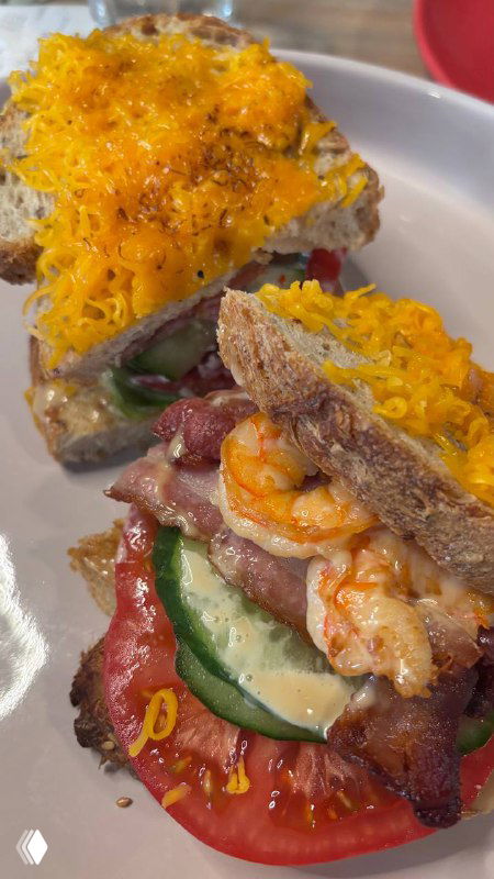 Крупный план сэндвича с креветками, свежими огурцами и томатом, сверху расплавленный сыр на ломте хлеба — аппетитный вид на тарелке в кафе.