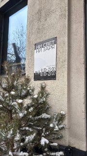 Фасад и табличка с названием «Ни свет ни заря» на стене здания, снежные ветви ели на переднем плане у входа в московское кафе.