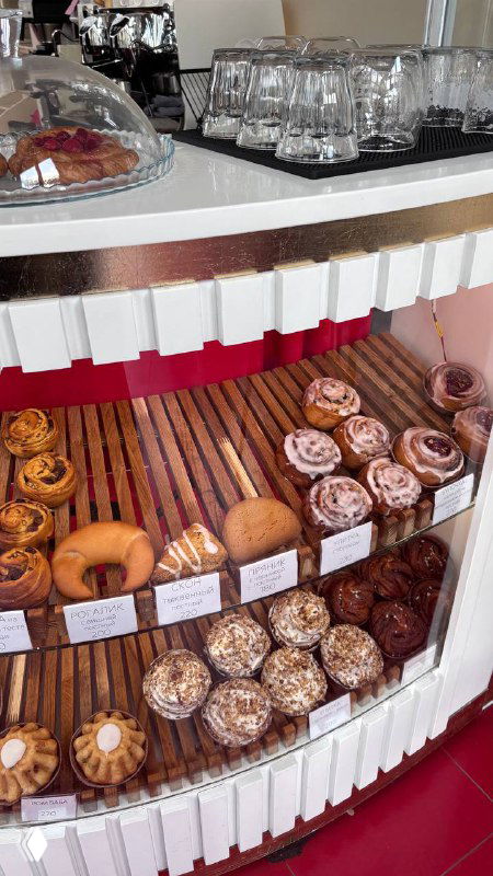 Витрина и стойка с сервированными бокалами и куполами для тортов; современная кофейная стойка в светлом помещении у храма.