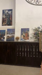 Декор и картины у стены в помещении трапезной: несколько полотен, цветочные композиции и тёмная деревянная панель внизу стены