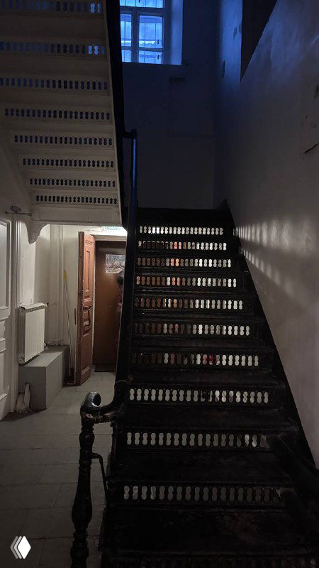 Тёмная деревянная лестница в старом помещении трапезной, вид на верхние витые перила и строгое архитектурное решение внутри здания.