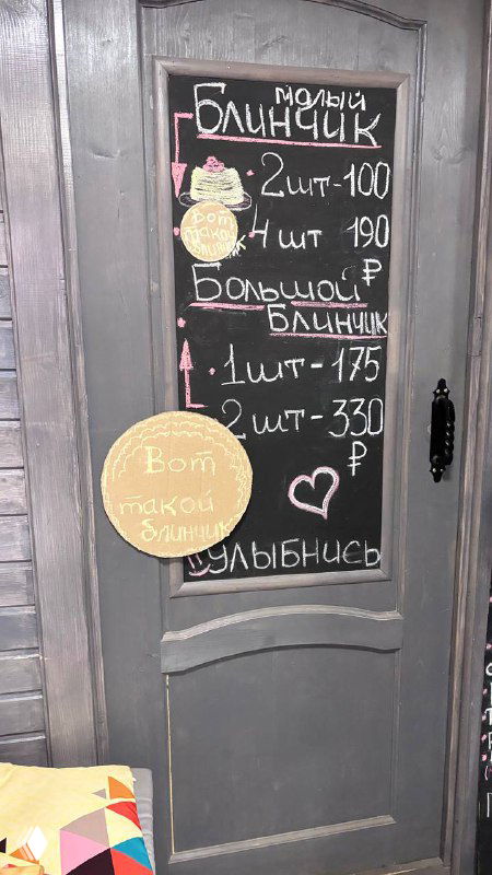 Дверь с меню на меловой доске: «малый блинчик 2шт» — фотография фасада или входа в маленькое блинное кафе в центре Москвы рядом с храмом.