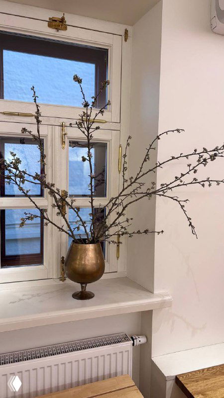 Бронзовая чаша с ветвями на подоконнике в светлой кофейне при храме — декоративный акцент в интерьере, окно и радиатор позади.