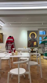 Интерьер трапезной при храме: столы и стулья на фоне икон и предметов церковного убранства; просторное помещение с высокими потолками.