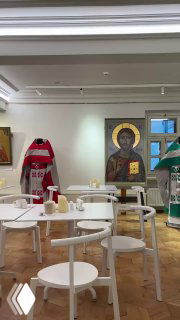 Интерьер трапезной при храме с иконами на стене и пустыми круглыми столиками — светлое помещение с религиозными элементами.