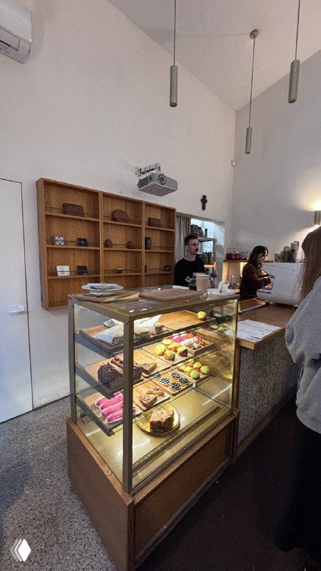 Витрина с кондитерскими изделиями в кофейне при культовом месте — стеклянная прилавочная витрина и барная зона за ней.