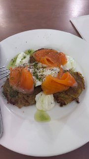 Блюдо с драниками, ломтиками рыбы и кусочками мягкого сыра на тарелке; крупный план еды на столе в кофейне при храме.