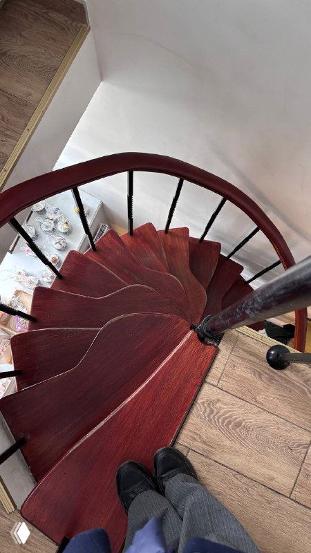 Вид сверху на винтовую лестницу: красные деревянные ступени и чёрные перила, фотография делает акцент на форме и глубине.