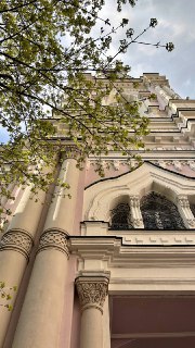 Низкий ракурс на фасад храма в Москве с колоннами, декоративными арочными окнами и ветвями дерева на переднем плане весной.