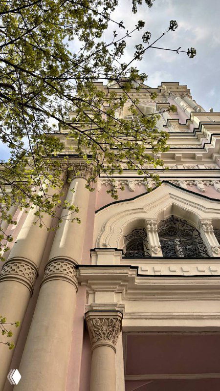 Крупный план фасада московского храма: колонны, арочные окна и лепнина, весенние ветви на переднем плане и голубое небо над зданием, архитектурный кадр.