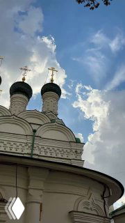 Купола православного храма с крестами на фоне голубого неба и облаков, ракурс снизу показывает бело-зелёную отделку и силуэты куполов.