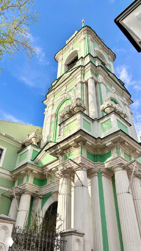 Колокольня с зелёными и белыми элементами фасада: пилястры, карнизы и декоративная отделка, снято при ярком дневном свете весны в Москве.