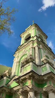 Фрагмент колокольни и фасада под углом, акцент на архитектурных деталях, ступенчатые ярусы и ясное весеннее небо.