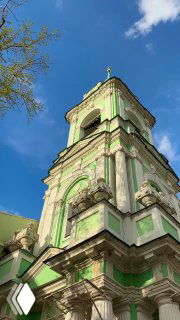 Боковой вид на колокольню с акцентом на текстуру стен и декоративные элементы, насыщенное синее небо и контрастная подсветка фасада в дневном свете.