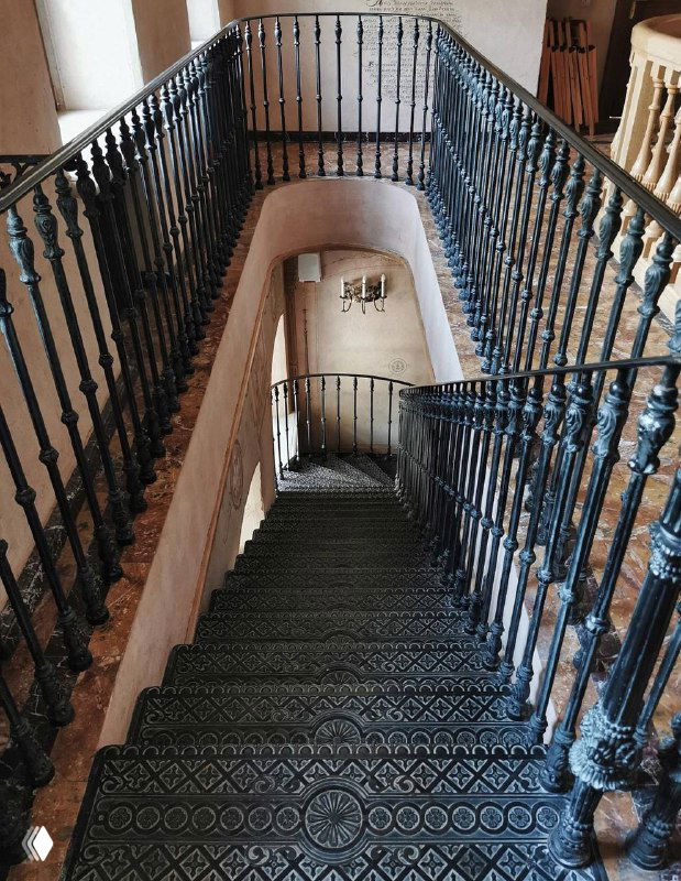 Винтовая чугунная лестница внутри старинного здания при храме: декоративные перила, узорные ступени и историческая фактура интерьера, интерьерный кадр.