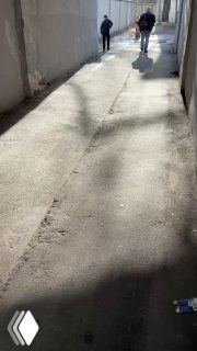 Узкий проход-арка во дворе храма с падающим светом и силуэтами прохожих, тени на бетоне и атмосфера спокойной городской прогулки весной.