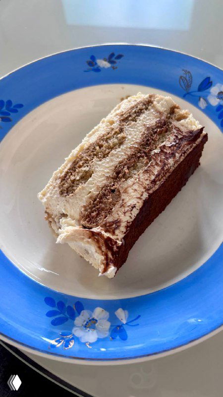 Кусок тирамису на синей тарелке: слоистый десерт с кремом и посыпкой, крупный план десерта в кафе «Лолита» в Москве.