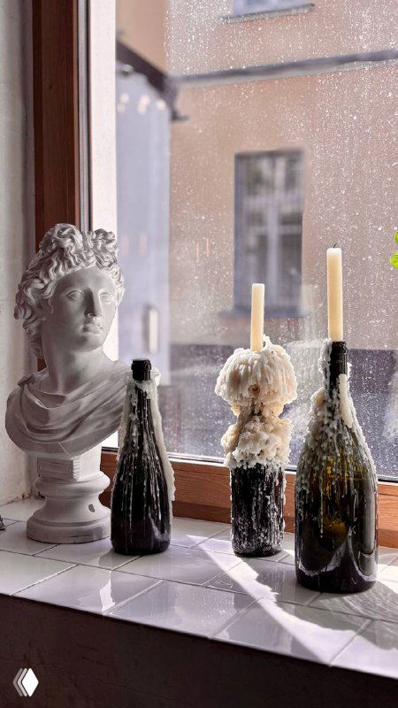 Подоконник кафе у окна с бутылками и застывшим воском от свечей; деталь интерьера, создающая уютную атмосферу заведения.