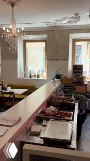 Буфет и стойка в интерьере кафе Публика: витрина с выпечкой и подносами с блюдами, столики и освещение на заднем плане.