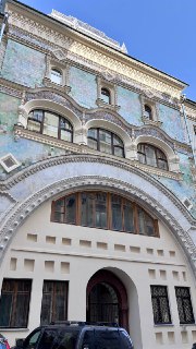 Крупный план арочной входной группы и декоративных элементов на фасаде жилого дома-колодца, видны орнаменты и окна над аркой.