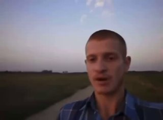 Размытый кадр: человек в клетчатой рубашке стоит на просёлочной дороге среди полей при сумерках, низкое качество фото, пейзаж на заднем плане.