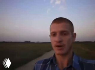 Размытое фото молодого мужчины на дороге в сельской местности на закате; кадр из видео, человек стоит на фоне поля и неба.