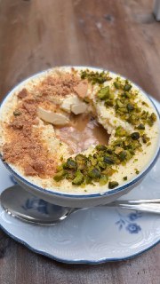 Чашка аффогато с кремовой пеной, крошками и фисташками, десерт на блюдце со столовой ложкой, близкий план