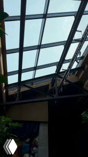 Фрагмент стеклянной крыши и металлических ферм над залом кафе: видно небо через стекло, конструкции и элементы декора интерьера.