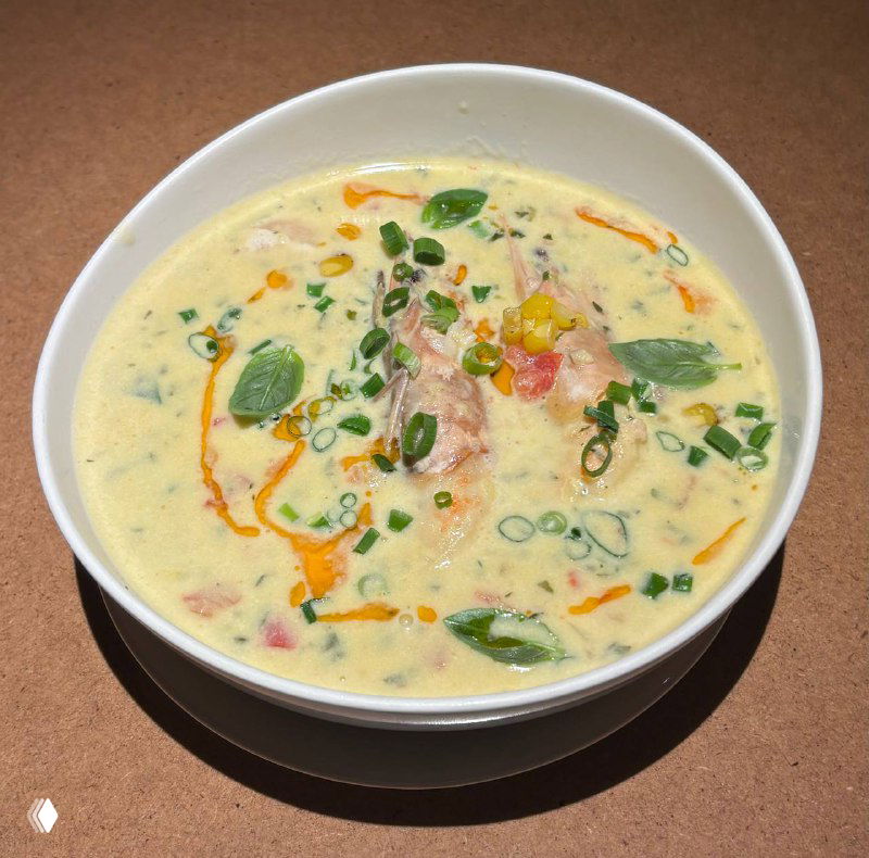 Тарелка сливочного клэм-чаудера с креветками и лососем, сверху зелень и сливочная текстура, подача в белой миске в ресторане.