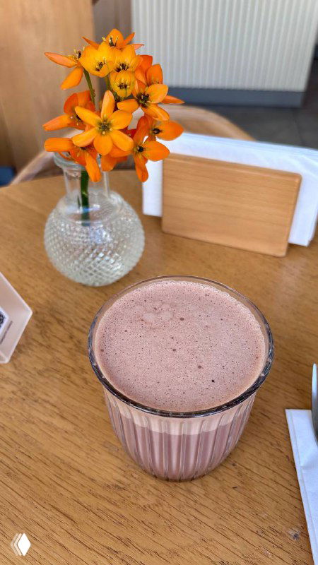 Какао или шоколадный напиток в стеклянном стакане на столе с небольшой вазой цветов и салфетницей — атмосферный кадр из интерьера Nobo.