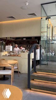 Интерьер кафе Nobo: открытая кухня, повара за барной стойкой, ступеньки и современный минималистичный дизайн в обеденное время.