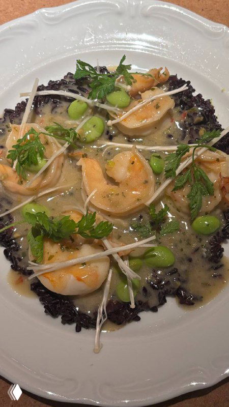 Креветки чака-лака, поданные на черном рисе с зелёными бобами, проростками и соусом, крупный план блюда в винном ресторане.