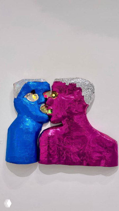 Скульптурная или настенная фигура в виде двух голов в ярких металлизированных синих и розовых тонах на белой стене музейного зала.