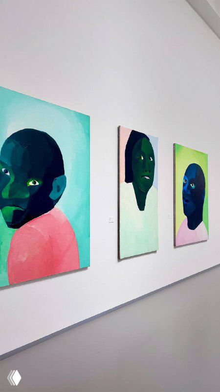 Ряд портретов на светлой стене: три картины с крупными стилизованными лицами в зелёно-розовой палитре, расставленные в линию.
