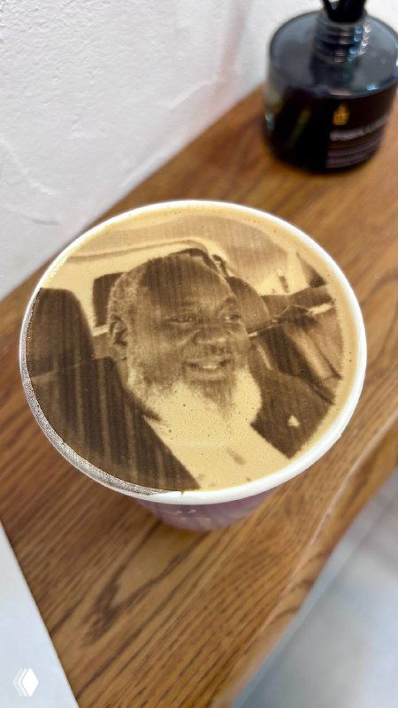 Крупный план латте-арта: на плотной пенке чашки отпечатано фото пожилого мужчины в коричневых тонах — принт на пенке вместо ожидаемого логотипа