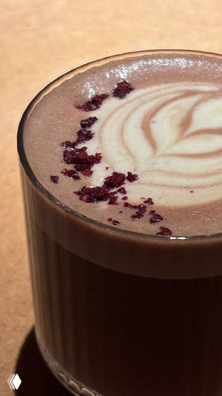 Стакан spicy rum какао с латте-арт и крошками ягод на поверхности, тёплый напиток в стеклянной посуде на столе ресторана.