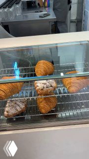 Витрина с несколькими круассанами и выпечкой на металлических решетках под подсветкой — свежая выпечка за стеклом