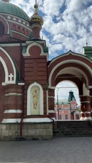 Фрагмент фасада православного храма с куполом и декоративными арками; кирпичная отделка, икона в нише и небо с облаками.
