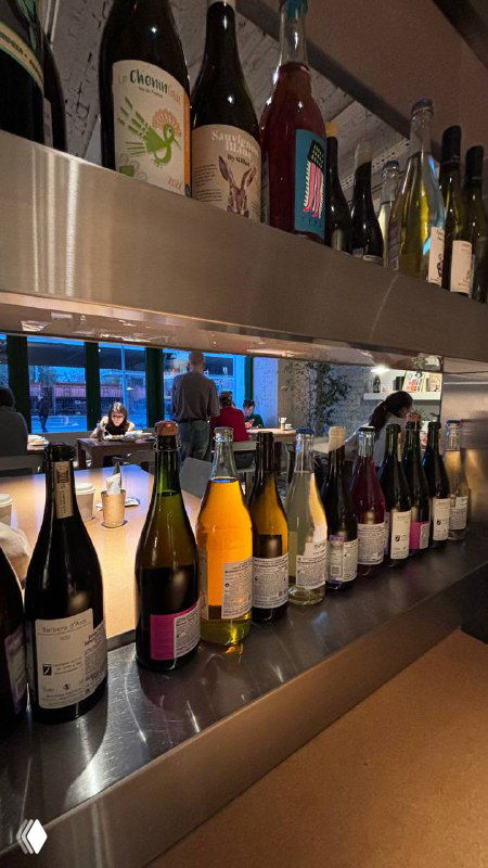 Ряд бутылок и натуральных вин на барной стойке ресторана, отражение в стекле и вид интерьера винного бара вечером.